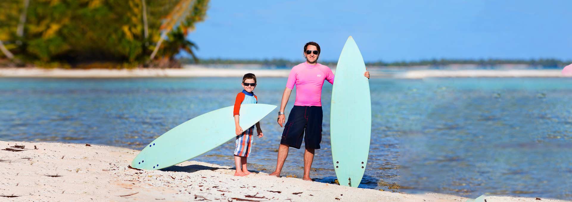 Father and son in rash guards with surfboards